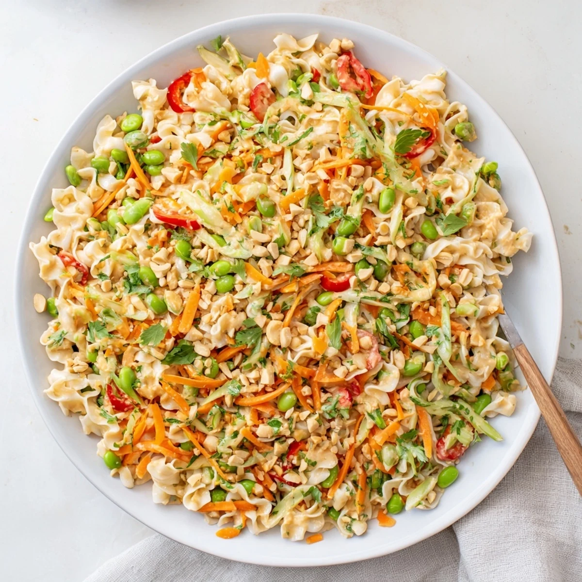 Steaming bowl of Spicy Peanut Noodle Salad with colorful veggies and a creamy dressing.