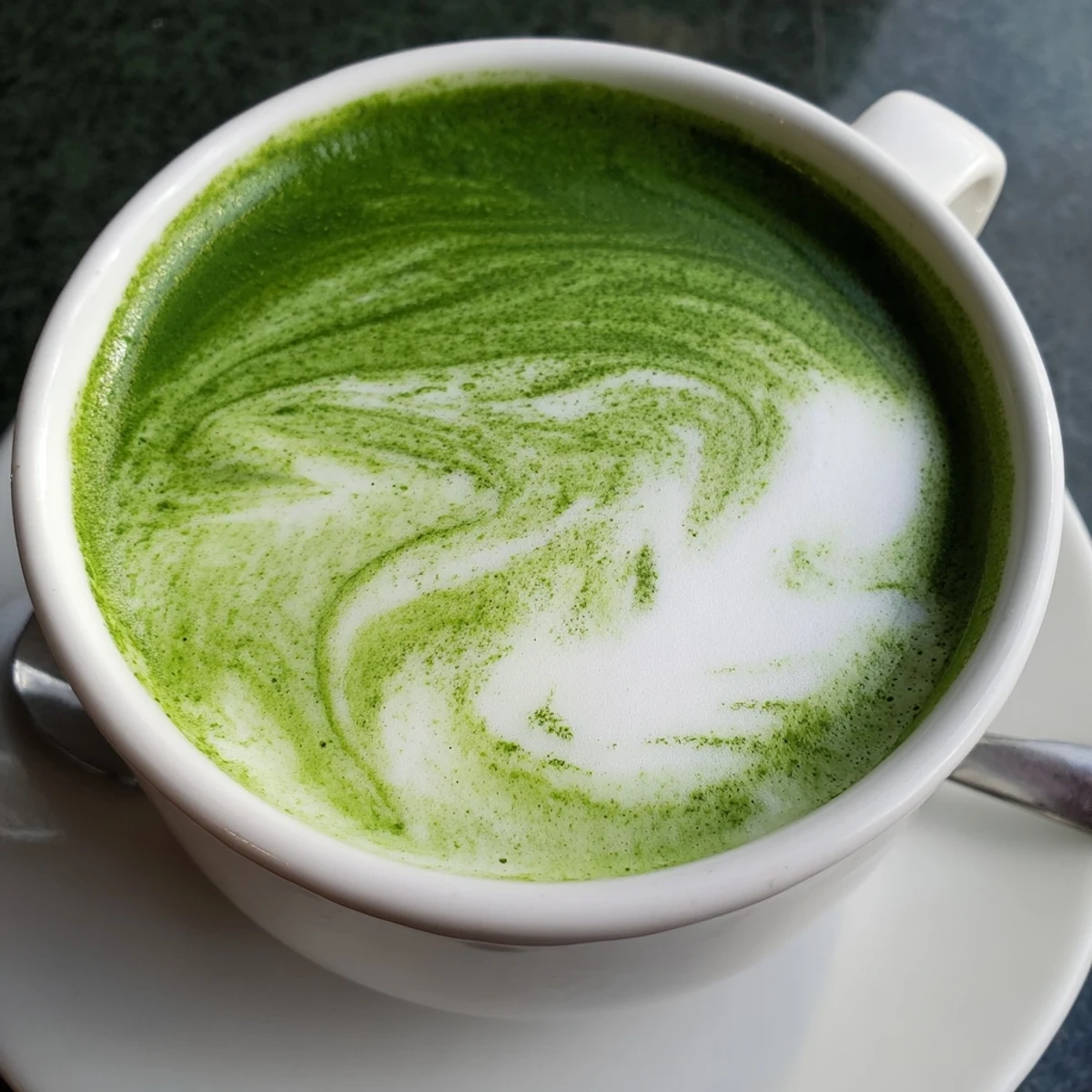 Steaming hot Matcha Green Tea Latte served in a white mug topped with delicate frothy milk foam.
