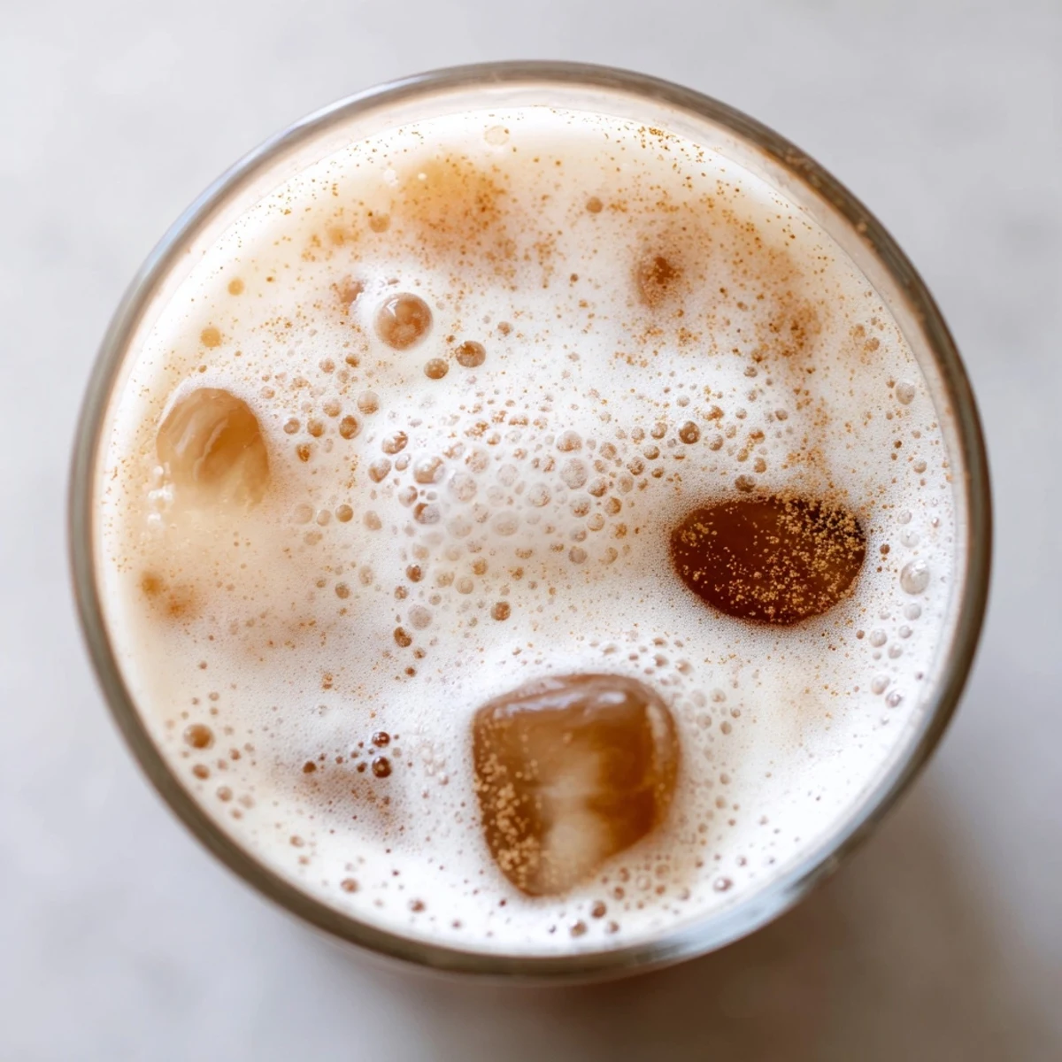 A close-up of two glasses of Iced Chai Tea with Cold Foam, garnished with ground cinnamon over the frothy top layer.