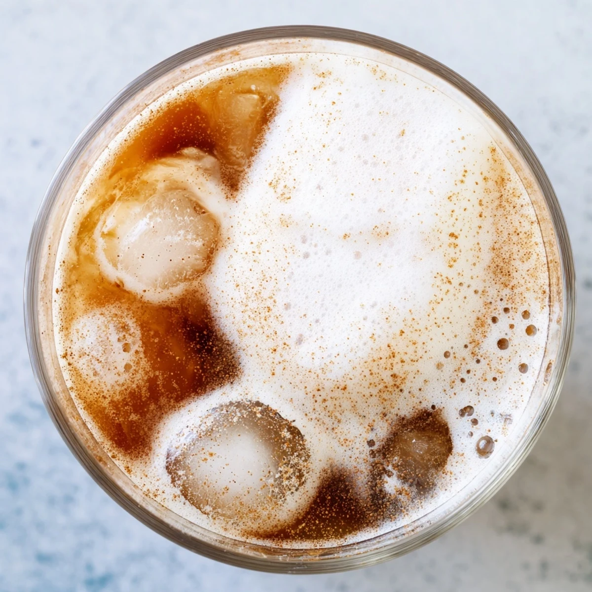 A top-down view of Iced Chai Tea with Cold Foam in a clear glass, highlighting the layered drink and cinnamon dusting.