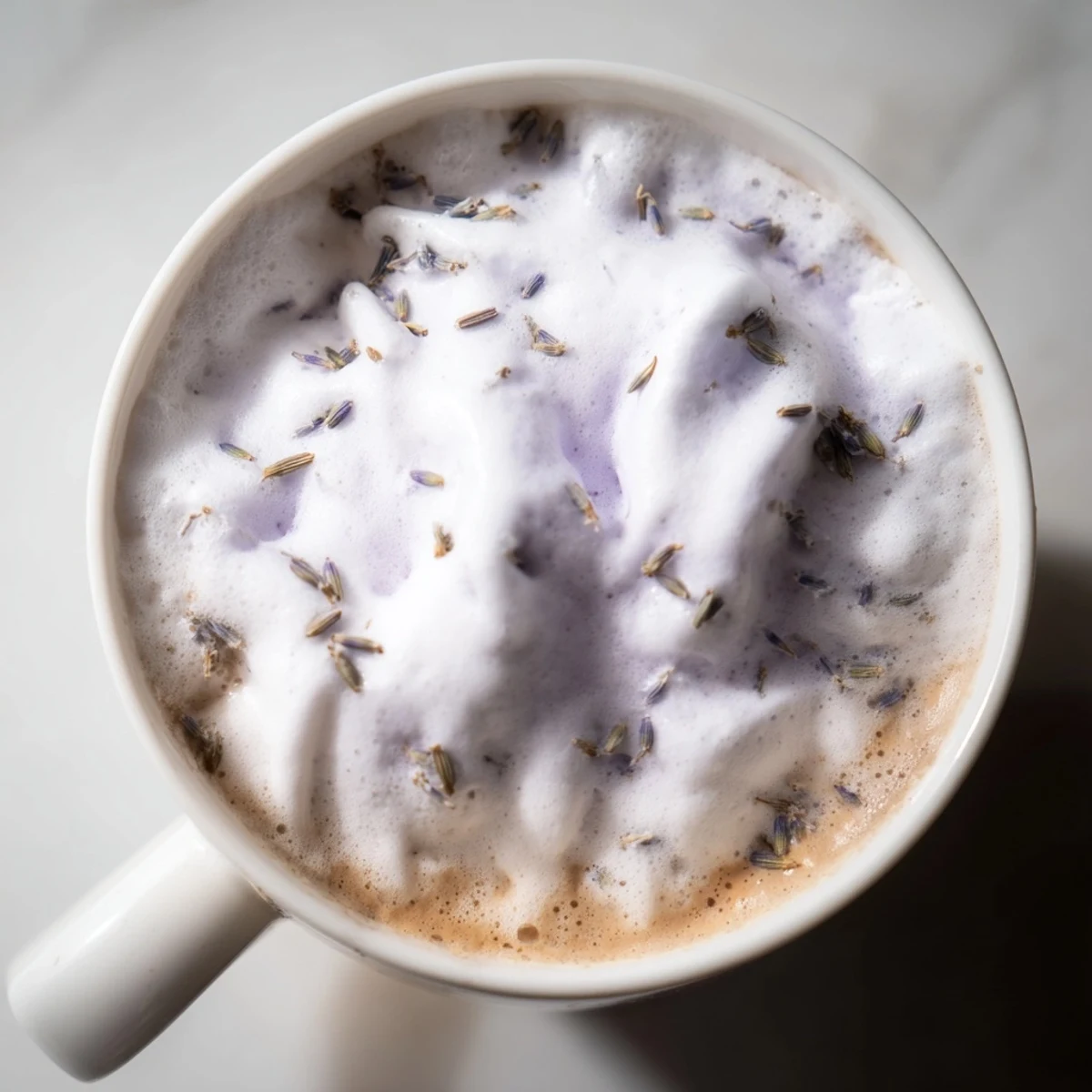 Two mugs of homemade Whipped Lavender Latte topped with swirls of fragrant foam and lavender buds.