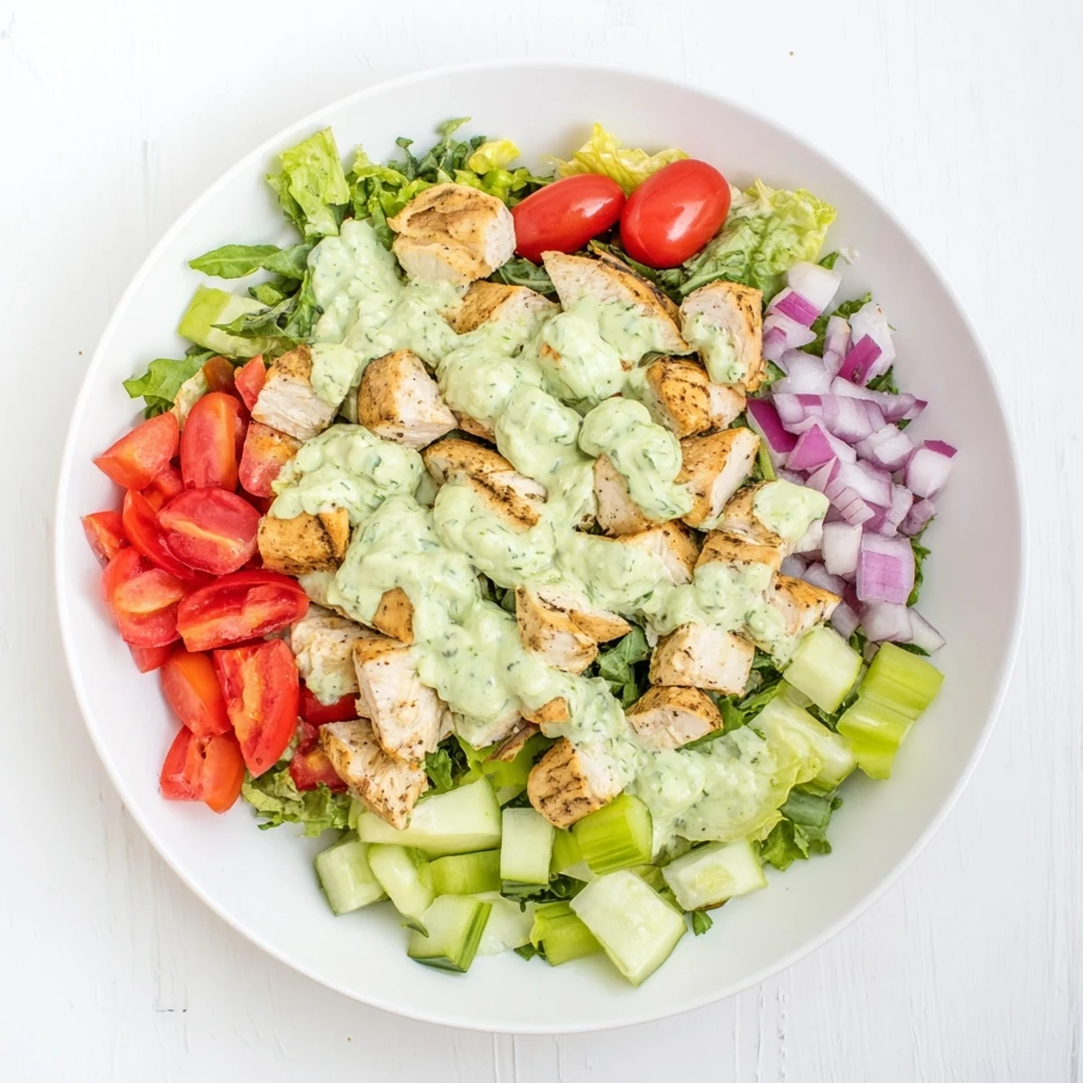 Sliced avocado ranch chicken salad served on a plate with herbs, cucumber, and cherry tomatoes, perfect for lunch or a light dinner.