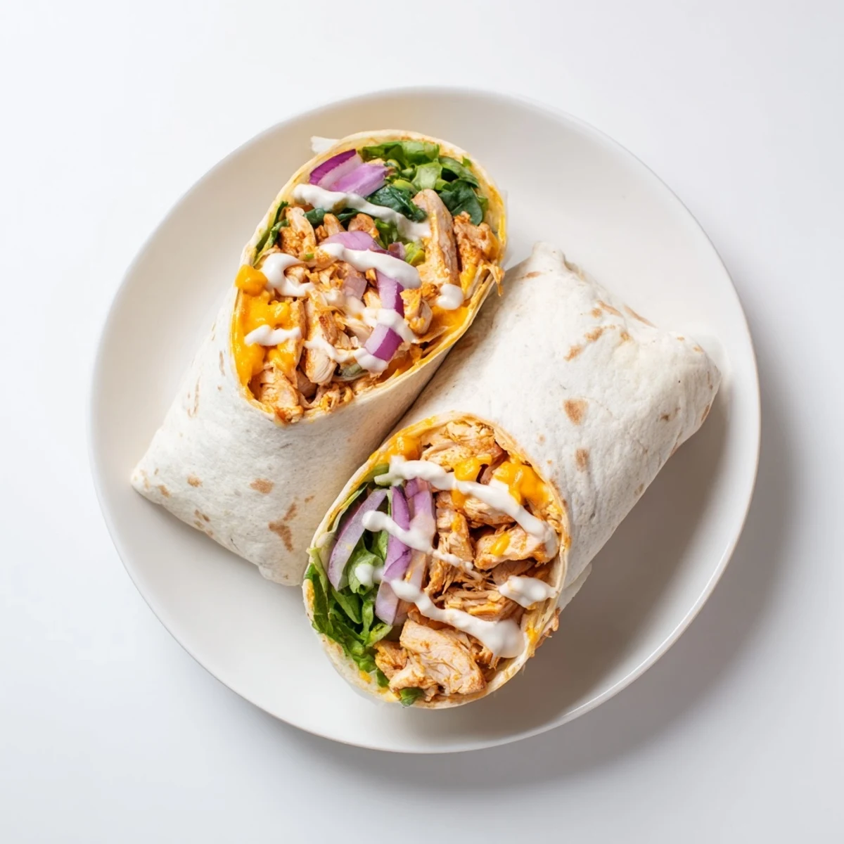Golden-brown toasted Buffalo Ranch Chicken Wrap sliced in half, revealing layers of romaine lettuce, shredded cheddar, and spicy chicken inside a whole wheat tortilla.  