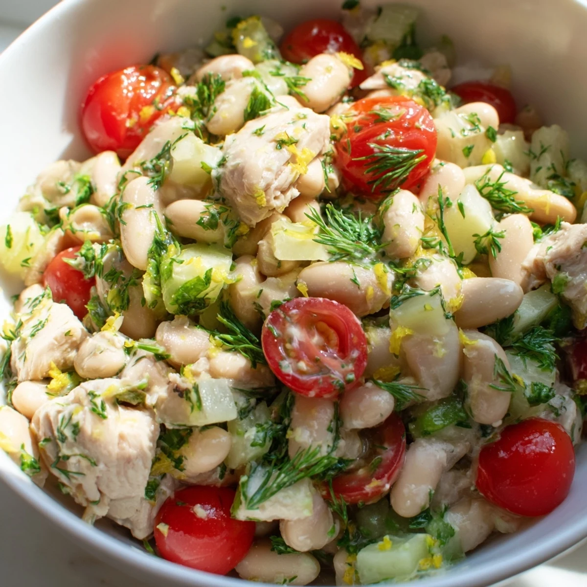 A bright Lemony White Bean Chicken Salad served over crisp lettuce, with halved cherry tomatoes, diced red onion, and a drizzle of zesty lemon dressing.