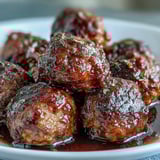 Juicy Slow Cooker Peach Glazed Meatballs studded with garlic and Parmesan, coated in a glossy orange glaze with flecks of red pepper.