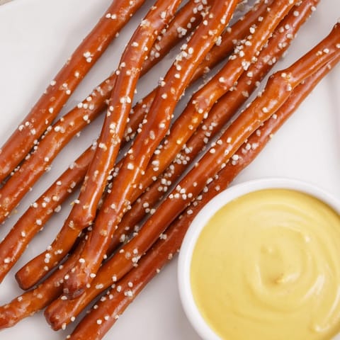 Close-up of golden pretzel rods and a bowl of spicy, homemade hot mustard dip.
