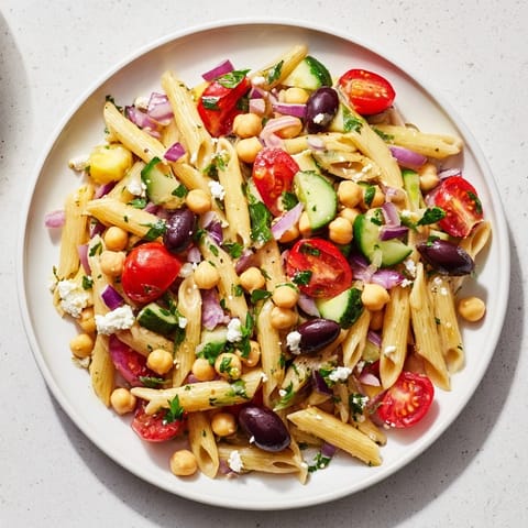 A colorful bowl of Mediterranean pasta salad with chickpeas, feta cheese, and fresh herbs, ready to serve.