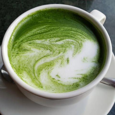 Steaming hot Matcha Green Tea Latte served in a white mug topped with delicate frothy milk foam.