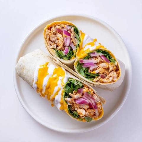 Juicy buffalo chicken, crisp romaine lettuce, and creamy ranch drizzle piled high on a fresh flour tortilla, ready to be rolled for dinner.  