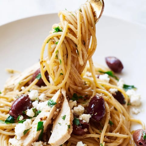 A skillet of freshly prepared Greek Chicken Spaghetti with juicy tomato slices, red onion, olives, and parsley, ready to serve on a white dinner plate.