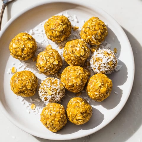 A hand reaches for a Ginger Turmeric Energy Ball beside a cup of herbal tea on a rustic wooden table.