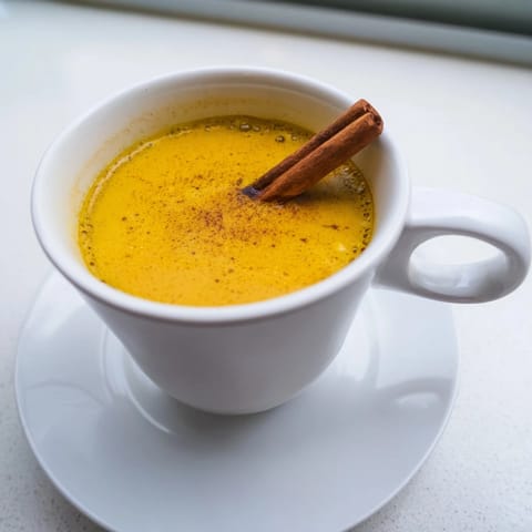 A top-down view of Turmeric and Ginger Golden Milk in a rustic mug, garnished with a cinnamon stick, ready to comfort on a cozy evening.  