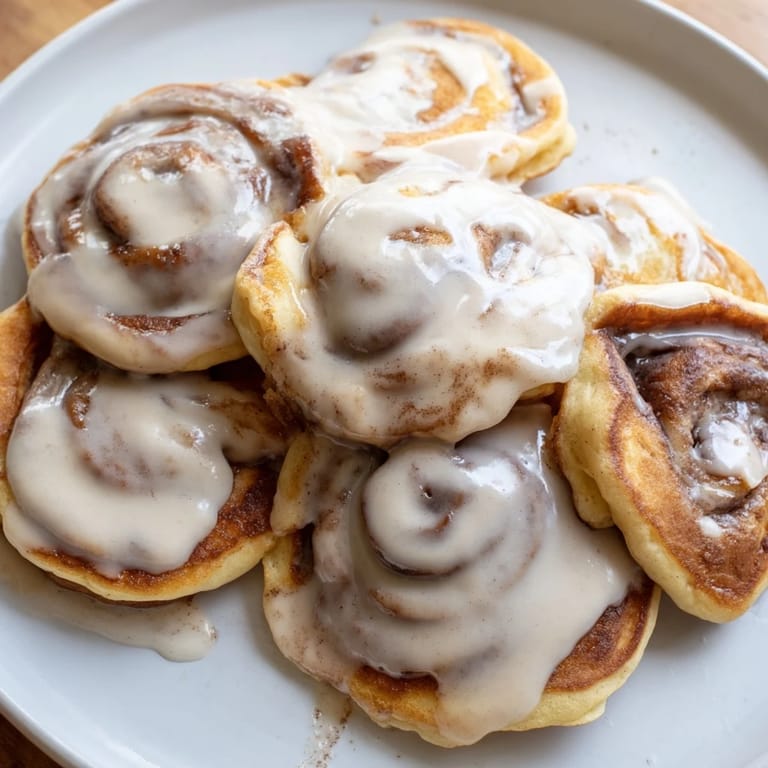 Warm, appetizing Cinnamon Roll Pancakes, perfectly stacked, ready to be devoured with sweet cream cheese.